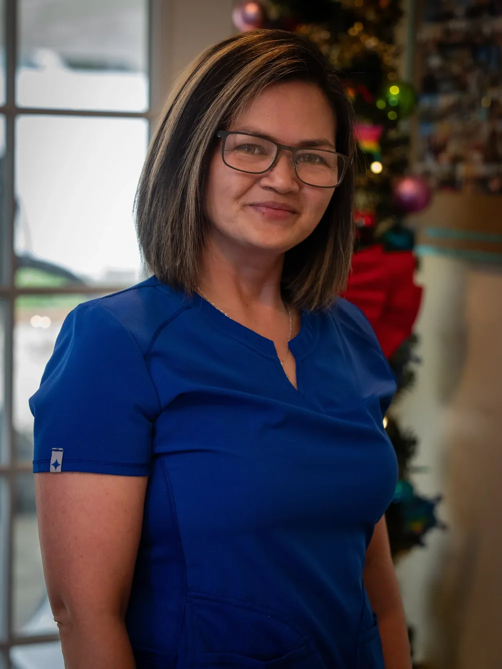 Smiling caregiver in blue scrubs wearing glasses in home care facility during holiday season